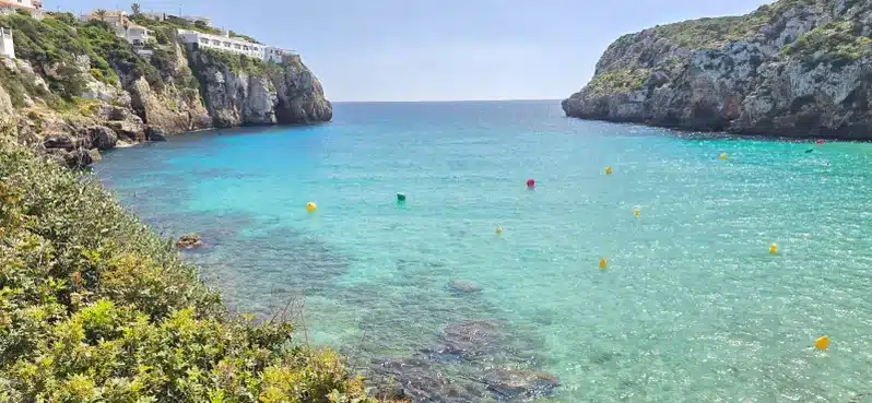 Muestra la cala den Porter en Menorca, con aguas azul turquesa y vegetación