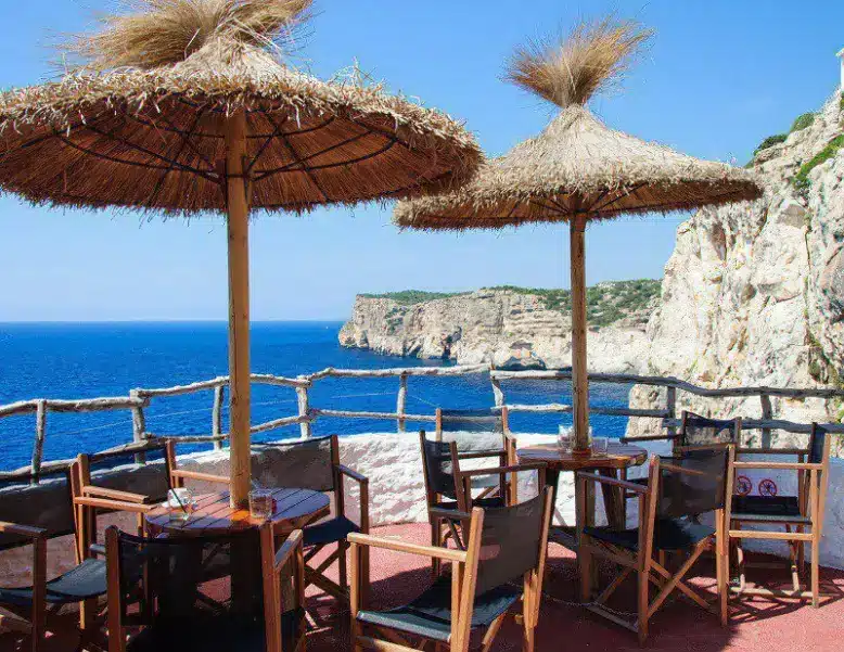 Se ve unas mesas con sombrilla y con vista al mar de La cova d’en Xoroi en Menorca