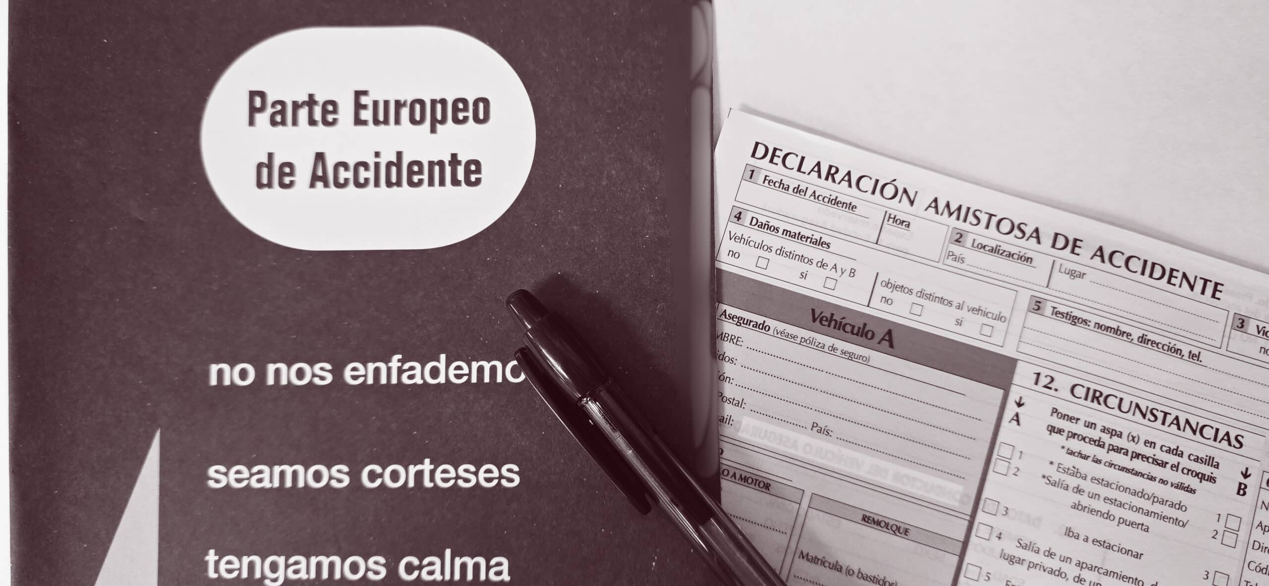 Cómo rellenar un parte amistoso de accidente sobre una mesa junto a un bolígrafo y folleto con recomendaciones de calma